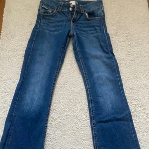 Blå lågmidjade bootcut jeans från Gina Tricot - Snygga blå jeans från Gina Tricot med klassisk femficksdesign och dubbla knappar i midjan. Perfekta för en avslappnad stil med en skön passform. De har en lätt tvättad look som ger en trendig touch.