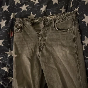 Grå jeans från Jack & Jones - Säljer ett par grå jeans från Jack & Jones i loose fit. De har en klassisk femficksdesign och knappar i gylfen. 28 i bredd och 32 i längd. De är ganska använda men väldigt bekväma och snygga. 