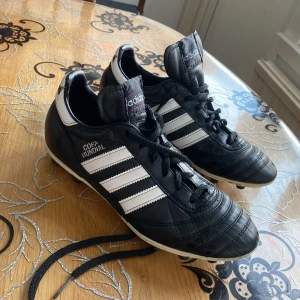 Adidas Copa Mundial fotbollsskor - Säljer ett par klassiska Adidas Copa Mundial fotbollsskor i svart och vitt. Skorna har snörning och är tillverkade i skinn för optimal komfort och hållbarhet. Perfekta för fotbollsplanen med sin tidlösa design och pålitliga prestanda.