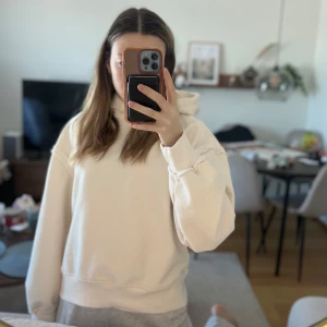 Beige hoodie med textdetalj, helt oanvänd  - Säljer en beige hoodie med en cool textdetalj på ryggen. Tröjan har långa ärmar och en avslappnad passform. Perfekt för en casual look. Hör av dig vid intresse!