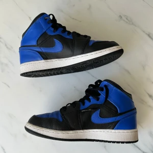 Nike Air Jordans i svart och blått - Snygga Nike Air Jordans i svart och blått med klassisk snörning. Skorna har en stilren design med perforerade detaljer på tån för extra ventilation. Perfekta för dig som vill ha en sportig och trendig look.