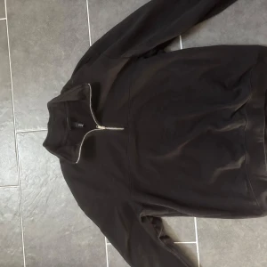 Svart tröja med dragkedja - Säljer en stilren svart tröja med dragkedja. Perfekt för en avslappnad look. Tröjan har långa ärmar och en hög krage med dragkedja framtill.