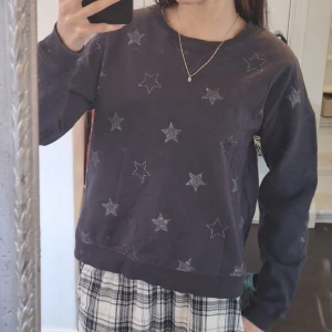 Mörkblå hoodie med stjärnmönster - Säljer en mörkblå hoodie utan luva med glittriga stjärnor. Tröjan har långa ärmar och en avslappnad passform. Perfekt för en mysig dag. Är I storlek 158-164 men ha S å den sitter perfekt.