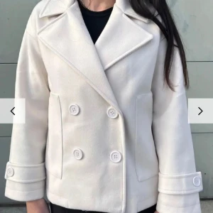 Design by si kappa - Snygg vit kappa med dubbelknäppning och bred krage från design by si i storleken s/m. Nypris runt 700kr 