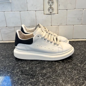 Alexander McQueen sneakers size 44 - Snygga vita sneakers från Alexander McQueen med en kontrasterande svart häl. Skorna har en tjock sula och klassisk snörning. Perfekta för en stilren look. Priset går att diskutera dem är lagade i hälen med hjälp av tejp och skumgummi utöver det bra skick på dem inget og finns kvar.