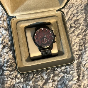 Svart klocka från Santa Barbara Polo & Racquet Club - Stilren klocka med svart mesharmband och vinröd urtavla. Klockan har tydliga markeringar och tre mindre urtavlor för extra funktionalitet. Levereras i en elegant svart förpackning. batteriet är slut