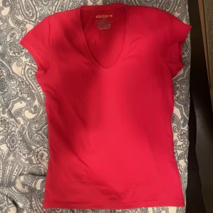 Rosa v-ringad topp från Abitare - Säljer en fin rosa v-ringad topp från Abitare i storlek S. Toppen är kortärmad och tillverkad i bomull med en liten del elastan för extra komfort. Den har en liten vit fläck på ryggen men den går nog bort i tvätten!