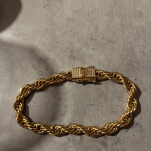 Guldarmband med tvinnad design - Elegant guldarmband med en tvinnad design och ett dekorativt lås. Perfekt för att ge en lyxig touch till din stil.