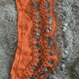 Orange dansbälte/magdans med silvermynt - Säljer ett snyggt orange dansbälte dekorerat med massor av silverfärgade mynt som klirrar när du rör dig. Perfekt för fest eller dansuppträdanden! Bältet är i bra skick och ger en härlig bohemisk känsla. Passar perfekt till sommarens alla fester. 🧡✨