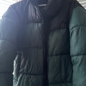 Svart och grön pufferjacka från Pull&Bear - Säljer en snygg svart och grön pufferjacka från Pull&Bear i mycket bra skick. Jackan har en dragkedja framtill och är perfekt för kalla dagar. Den är varm och bekväm, idealisk för både höst och vinter. Passar perfekt för en casual look! Storlek: S men funkar också för M