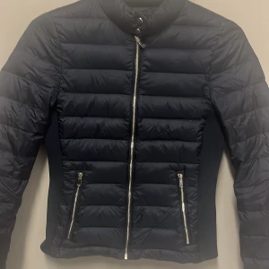 Marinblå dunjacka från Zara Woman - Säljer en snygg marinblå dunjacka från Zara Woman i storlek XS. Jackan har en stilren design med dragkedja framtill och två praktiska fickor med dragkedjor. Perfekt för kyliga höst- och vinterdagar. Den är i mycket bra skick och redo för nya äventyr! 🖤