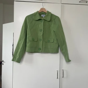 Grön kavaj med stora knappar &Other Stories  - Säljer en snygg grön kavaj i bra skick. Den har stora knappar framtill och två fickor med lock. Materialet känns mjukt och bekvämt, perfekt för vår och höst. Passar bra till både vardag och festliga tillfällen. Storleken är inte angiven men verkar vara normal passform.
