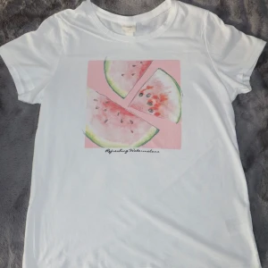 Vit t-shirt med vattenmelontryck -  it t-shirt med ett färgglatt tryck av vattenmelonskivor på framsidan. T-shirten är kortärmad och gjord i mjukt bomullsmaterial. Den är i bra skick!
