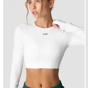 Vit croppad topp från ICANIWILL - Snygg och stilren vit croppad topp från ICANIWILL. Perfekt för träning eller en sportig look. Den har långa ärmar och en öppen rygg som ger en cool touch. Materialet är stretchigt och bekvämt, vilket gör den idealisk för aktiva dagar. Helt oanvänd med lapp kvar