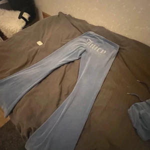 Blå velourbyxor från Juicy Couture - Säljer ett par snygga blå velourbyxor från Juicy Couture i storlek M. Byxorna har en bekväm passform och är perfekta för en avslappnad stil. De har en bredare bootcut-stil och är supermjuka och sköna att ha på sig. Perfekta för mysiga dagar hemma eller en chill dag ute.