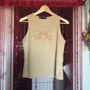 Beige ärmlös topp från Saint Tropez - Snygg beige ärmlös topp från Saint Tropez med texten 'Madonna Rock' och coola gitarrer i glittriga detaljer. Perfekt för en rockig look eller en avslappnad dag ute. Toppen är i ett mjukt och bekvämt material.