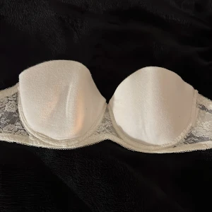 Vit axelbandslös BH från H&M 75B - Vit axelbandslös BH från H&M i storlek 75B. Den har en vacker spetsdetalj på sidorna. Bra skick