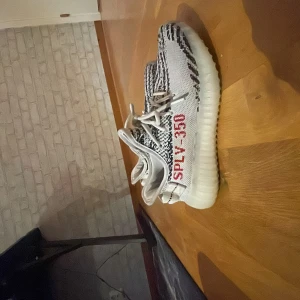 Adidas Yeezy Zebra - Säljer ett par Adidas Yeezy i Zebra-mönster. De är i mycket bra skick och har den klassiska vita och svarta designen med röd text på sidan. Perfekta för både vardag och fest! Storlek 38-39