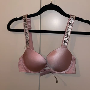 Rosa bh från Victoria's Secret - Säljer en superfin rosa bh från Victoria's Secret. Den har glittriga axelband som verkligen sticker ut och ger en lyxig känsla. Materialet är mjukt och skimrande, perfekt för en festlig kväll. Bh:n är i mycket bra skick och ALDRIG använd. Har även i röd, blå och svart