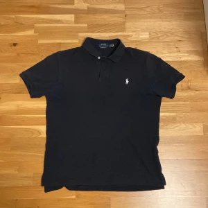 Svart pikétröja från Ralph Lauren - Säljer en klassisk svart pikétröja från Ralph Lauren i storlek M. Tröjan har en broderad logga på bröstet och är i ett custom slim fit. 