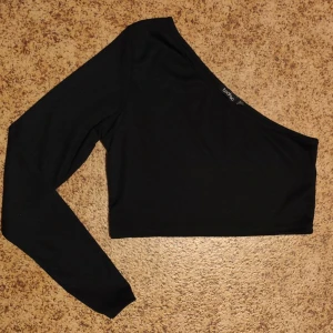 Svart oneshoulder topp från Boohoo - Snygg svart oneshoulder topp från Boohoo i ett mjukt och stretchigt material. Perfekt för en utekväll eller fest! Toppen har en lång ärm och en stilren design som gör den lätt att matcha med olika outfits.