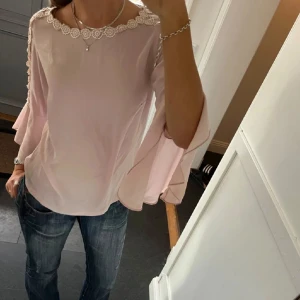 Ljusrosa blus med spetsdetaljer - Säljer en superfin ljusrosa blus med vackra spetsdetaljer vid halsen och på ärmarna. Blusen har långa, fladdriga ärmar som gör den perfekt för både vardag och fest. Den är i mycket bra skick och passar perfekt till jeans eller kjol. (Köpte från tjejen på bilden men den passa inte mig så säljer vidare) 