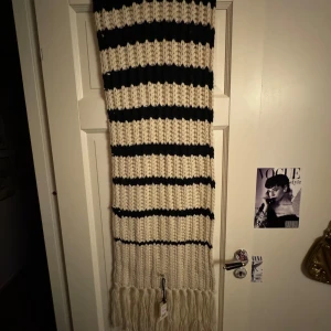 Randig stickad halsduk från Jean Paul Gaultier by Lindex - Säljer en superfin och mysig stickad halsduk från Jean Paul Gaultier. Den är randig i blå och vit med fransar i ändarna. Perfekt för att hålla sig varm och stilren under de kallare månaderna. Passar till alla outfits och är ett måste i garderoben.