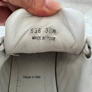 Vita sneakers från Prada - Säljer ett par stilrena vita sneakers från Prada i storlek 36. Skorna är tillverkade i Italien och har en klassisk design med snörning och en diskret logga på hälen. De är i bra skick och perfekta för både vardag och fest. Passar till alla säsonger och ger en lyxig touch till din outfit.