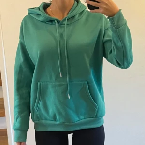 Grön hoodie - Säljer en supermysig grön hoodie i storlek M. Den har en klassisk design med en stor ficka fram och justerbar dragsko i huvan. Perfekt för chilliga dagar eller när du bara vill vara bekväm. Passar både till vardags och för en avslappnad stil.