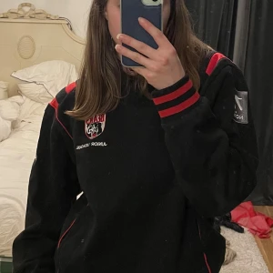 Svart och röd tröja med logga - Säljer en svart tröja med röda detaljer och en cool logga på bröstet. 