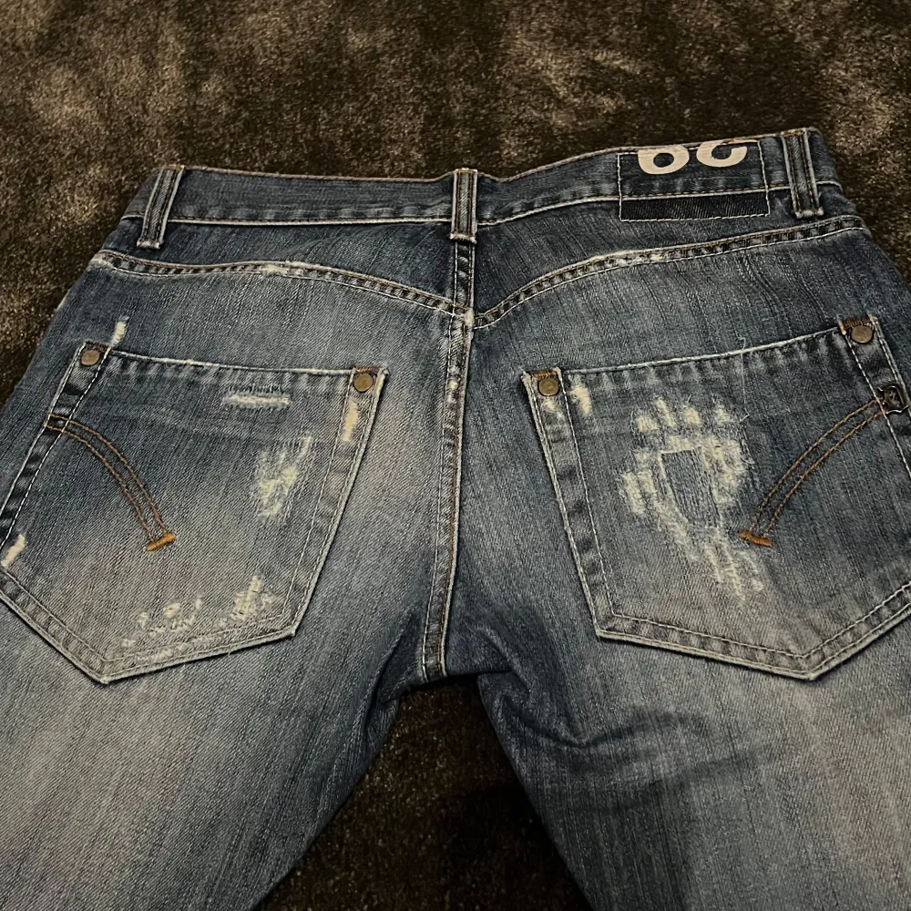 Säljer ett par snygga blå jeans från Dondup i storlek 29. De har en cool sliten look med ljusa slitningar på både fram- och baksidan. Jeansen har en klassisk femficksdesign och är perfekta för en avslappnad stil. Passar både till vardags och fest!. Jeans & Byxor.