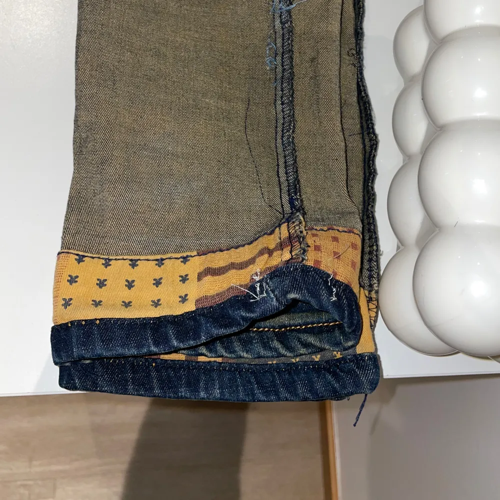 Säljer ett par blå jeans med coola slitningar och en unik insida med mönster. Jeansen har en klassisk blå färg och är i en välanvänd stil med slitna detaljer som ger dem en edgy look. Insidan av byxorna har ett rutigt och mönstrat tyg i beige och brunt, vilket gör dem extra speciella.. Jeans & Byxor.