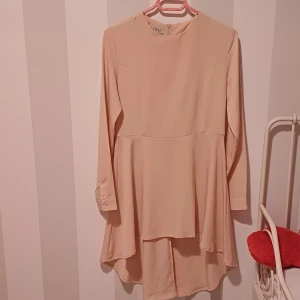 Klänning - Säljer en superfin beige klänning från Y.A.S. Den har långa ärmar och en lös passform som ger en skön och avslappnad känsla. Perfekt för både vardag och fest! Klänningen har en enkel design med en liten dragkedja i ryggen.