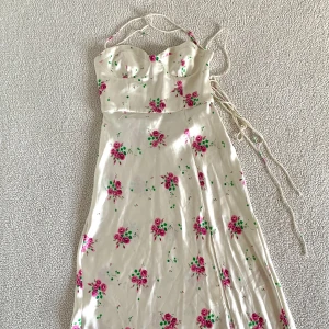 ZARA blommig vacker satinklänning med slits och snörning - Otroligt vacker krämvit satinklänning från ZARA med blommor och slits. Öppen rygg med snörning i ryggen och dold dragkedja. Endast använd i några timmar, utan anmärkningar. Ordinariepris 599kr.