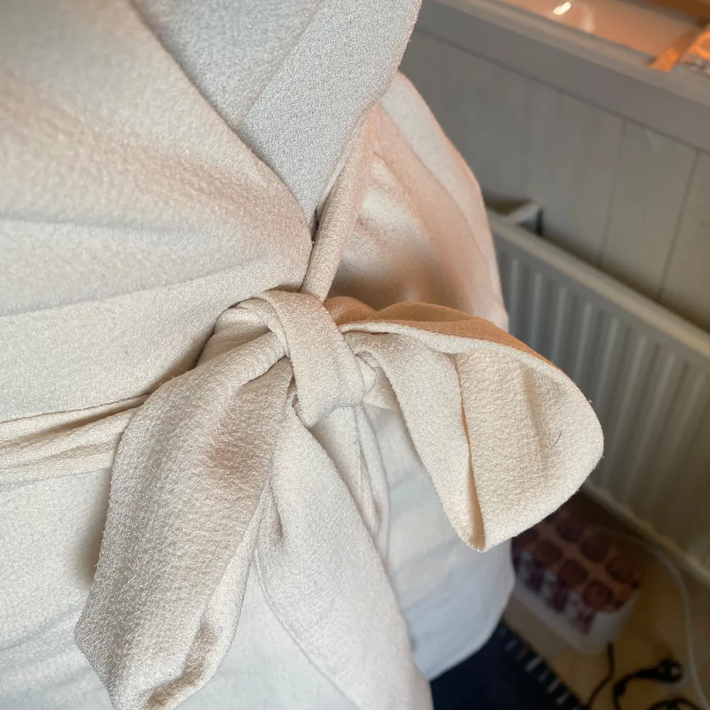 creme färgad/vit, (tunn), kavaj/jacka med knytband i midjan. Den har en klassisk krage och långa ärmar, perfekt för både vardag och fest. använd få gånger och passar både XS och S. Takit.