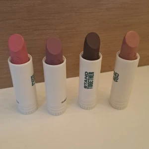 Fyra läppbalsam i olika nyanser - Säljer ett set med fyra läppbalsam i olika färger. Förpackningarna är vita med inspirerande texter som 'SHOW LOVE', 'SPEAK UP', 'STAND TOGETHER' och 'BE YOU'. Färgerna på läppbalsamen är rosa, lila, brun och nude. Perfekt för att hålla läpparna mjuka och återfuktade med stil!