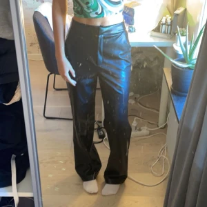 Svarta byxor från ASOS Design - Säljer ett par svarta byxor från ASOS Design. De är högmidjade och har en rak passform som ger en stilren look. Byxorna är gjorda i ett syntetmaterial som ger en glansig finish. Perfekta för både vardag och fest! Upplever dem något stora i storlek.