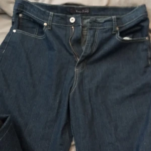 Jeans - Ett par mörkblåa jeans i storlek 44. Det är ett par mamma-jeans så de sitter lite lös vid låren ner till fötterna. De sitter bra vid midjan. Har nästan aldrig använt de, då jag föredrar andra jeans istället.