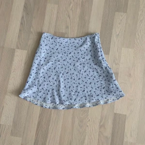 Sommar kjol - En blå kjol med blommor på från H&M. Jag har klippt bort lappen som ska vara på men är väldigt säker på att den är i storlek xxs-xs. Runt 32 cm bred upptill och 40 cm lång. Bara använts några få gånger.