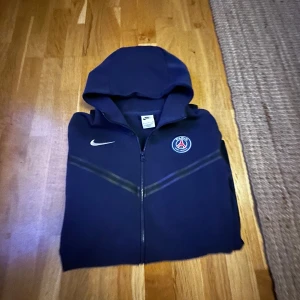 En Paris Nike tech tröja  - En PSG tröja i mörkblå färg som jag har använt runt 5 gånger men som jag inte behöver längre så jag säljer den i storlek S. Pris kan diskuteras om ni vill