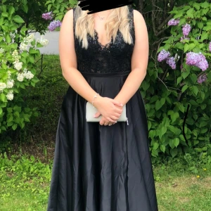 Svart långklänning med spetsdetaljer - Säljer min svart långklänning från JJs House med v-ringad spetsöverdel och ärmlös design. Kjolen har en stilren slits, den har även två fickor på vardera sida och är uppsydd på nedre delen av klänningen. Den är även bara använd en gång och är i väldigt gott skick😊Köptes för 2000kr med frakt, priset kan diskuteras. 