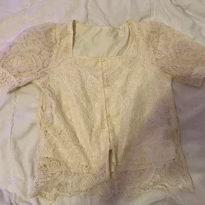 Beige spetsblus - Säljer en romantisk beige spetsblus med korta ärmar och knappar framtill. med ett vackert mönster och en feminin touch. Blusen har en fyrkantig halsringning och är i mycket bra skick.säljs för 50