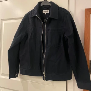 Svart jacka från Weekday - Säljer en snygg svart jacka från Weekday i nytt skick med prislapp kvar. Den har en stilren design med dragkedja framtill och knappar vid ärmsluten. Perfekt för både vår och höst. Jackan är i storlek S och passar till många olika outfits.