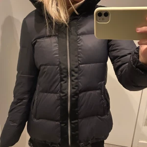 Svart dunjacka med dragkedja - Säljer en snygg och varm svart dunjacka. Perfekt för kalla dagar. Jackan har en normal passform och långa ärmar. Den är i mycket bra skick!