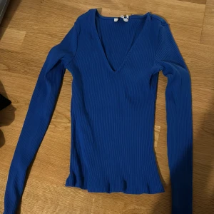 Blå ribbad topp från NA-KD - Säljer en snygg blå ribbad topp från NA-KD i storlek XS. Toppen har en v-ringad design och långa ärmar, perfekt för både vardag och fest. Materialet är stretchigt och bekvämt, vilket gör den idealisk för alla säsonger. Passar perfekt med jeans eller kjol för en stilren look.