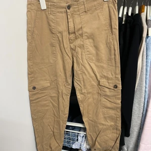 Beige cargobyxor från 157 - Säljer ett par beige cargobyxor från 157 i storlek M. Byxorna har flera praktiska fickor med knappar och en dragkedja framtill. Perfekta för en avslappnad stil och passar bra till vardags. De är i bra skick och redo för nya äventyr!