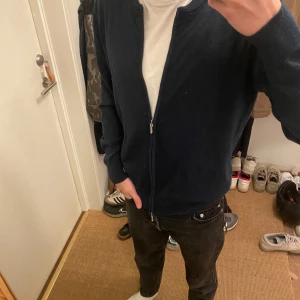 Mörkblå kofta från Grand Frank - Säljer en snygg mörkblå kofta från Grand Frank, tillverkad i Italien. Den har en dragkedja framtill och är perfekt för både vardag och lite finare tillfällen. Koftan är i storlek Large men är som en small och passar perfekt för höst och vår. 