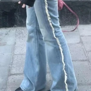 Ljusblå jeans med fransdetaljer - Säljer ett par ljusblå jeans från weekday med coola fransdetaljer längs sidorna. De har en bootcut-stil och är lågmidjade, Perfekta för både vardag och fest! 🕺heöt slutasålda. Innerbenslängd 85 cm. Och midja rakt över 37.5 cm