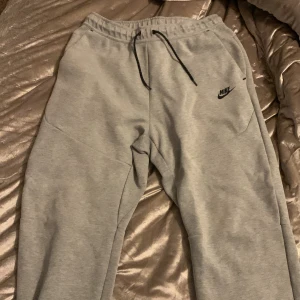 Grå mjukisbyxor från Nike - Säljer ett par grå mjukisbyxor från Nike i storlek L. De är superbekväma med elastisk midja och dragsko för perfekt passform. Perfekta för chill dagar eller träning. Byxorna har fickor på sidorna och en diskret Nike-logga på ena benet. Grymt sköna och stilrena!