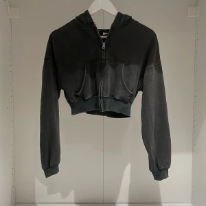 Svart/grå croppad hoodie från Divided - Säljer en svart/grå croppad hoodie från Divided by H&M. Den har en dragkedja framtill och en mysig huva. Perfekt för en avslappnad stil och passar bra till både jeans och leggings. Perfekt för höst och vår!